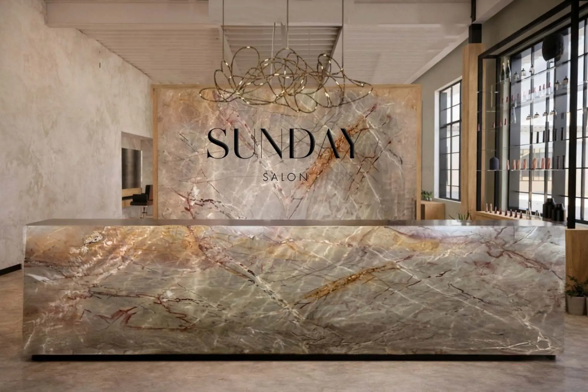 A modern salon reception area with a large, marble front desk and wall, displaying the words "SUNDAY SALON." Elegant lighting hangs above, and shelves with products are visible by tall windows.