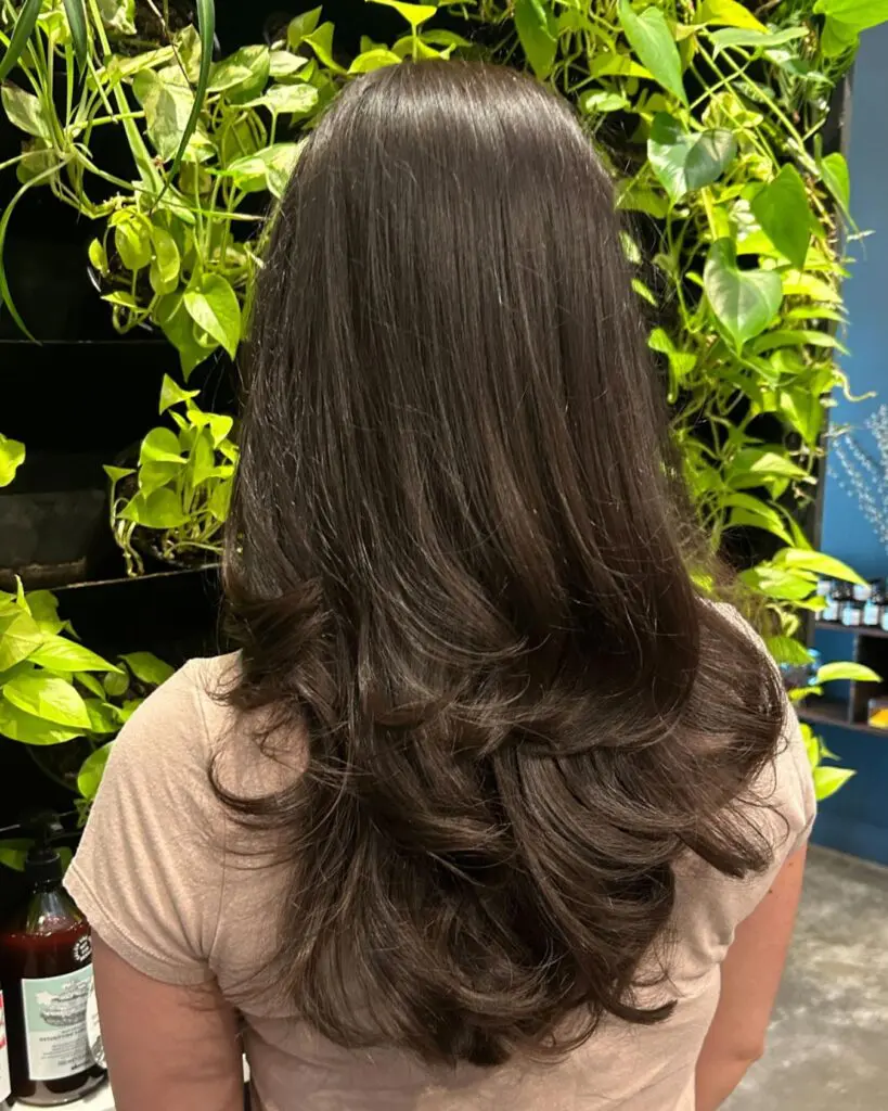 Lush Dark Chocolate Brunette with Bouncy Volume Layers A client with thick, long dark chocolate brunette hair styled in a voluminous blowout with bouncy, highly textured layered ends at Sunday Salon in Raleigh.