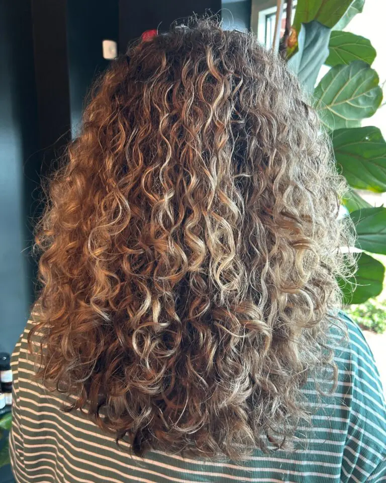 A client showcasing long, highly textured natural curls featuring dimensional golden honey highlights and expert curl definition styling at Sunday Salon in Raleigh.