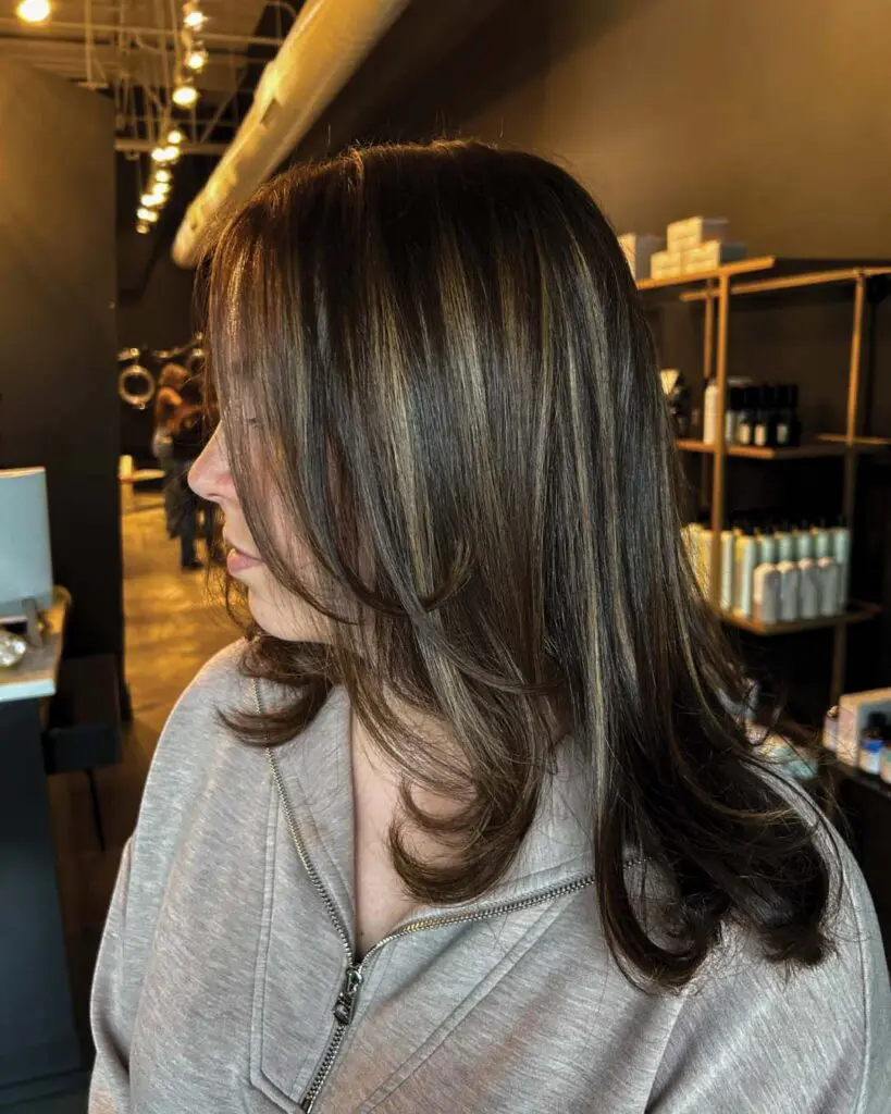Dimensional Warm Brunette with Soft Caramel Highlights and Face-Framing Layers Medium-length dark brunette hair styled sleekly with face-framing layers and striking dimensional caramel highlights, expertly crafted by a stylist at Sunday Salon in Raleigh.