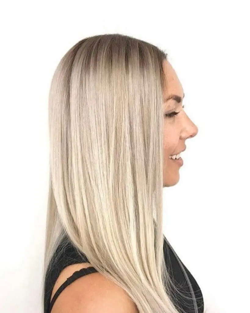 Icy Platinum Blonde with a Seamless Root Shadow and Sleek Finish Profile view of a smiling woman with long, sleek, pin-straight icy platinum blonde hair featuring a seamless dark root shadow by Lisa Edwards at Sunday Salon in Raleigh, NC.