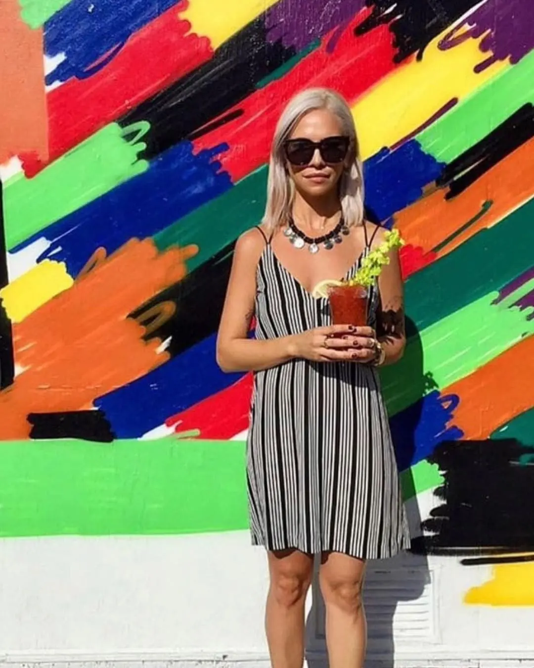 Icy Platinum Lived-In Blonde Lob with a Striking Root Shadow A woman standing in front of a colorful mural showcasing a sleek, shoulder-length icy platinum blonde lob with a dark root shadow by Lisa Edwards at Sunday Salon in Raleigh, NC.