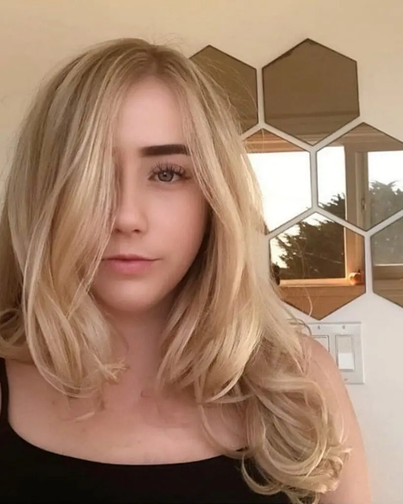 Creamy Vanilla Blonde with a Soft Shadow Root and Sweeping Face-Framing Layers Portrait of a woman with medium-long creamy vanilla blonde hair styled with a deep side part and soft curls at the ends, featuring a shadow root by Lisa Edwards at Sunday Salon in Raleigh, NC.