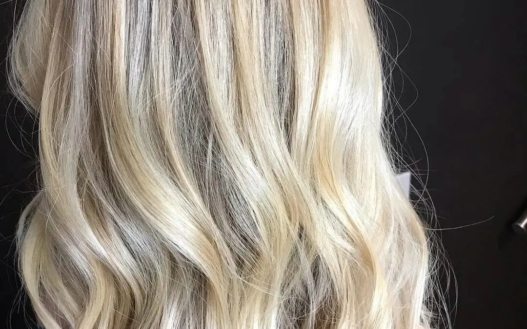 Back view of a woman with medium-long bright pearl blonde hair styled in loose waves, featuring a subtle shadow root by Lisa Edwards at Sunday Salon in Raleigh, NC.