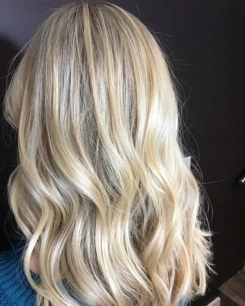 Back view of a woman with medium-long bright pearl blonde hair styled in loose waves, featuring a subtle shadow root by Lisa Edwards at Sunday Salon in Raleigh, NC.