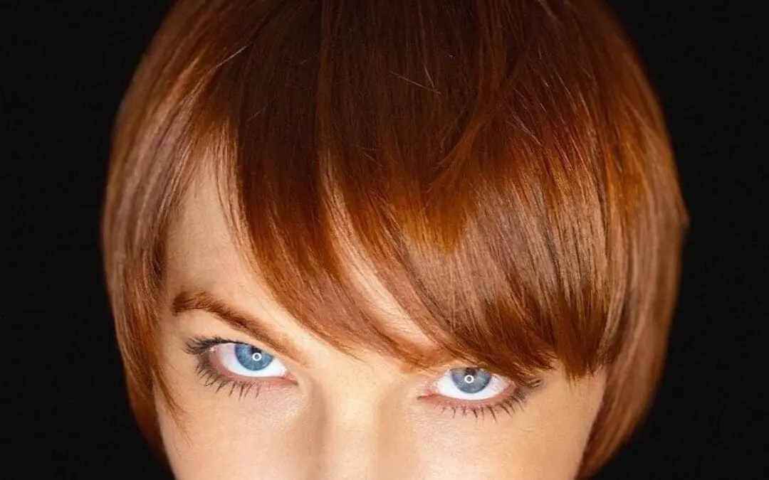 Close-up portrait of a woman with a sleek short pixie cut and sweeping front fringe, featuring a vibrant copper red all-over color by Lisa Edwards at Sunday Salon in Raleigh, NC.