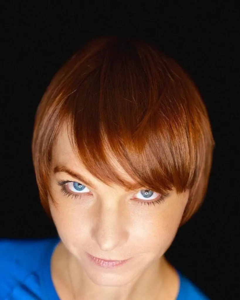 Close-up portrait of a woman with a sleek short pixie cut and sweeping front fringe, featuring a vibrant copper red all-over color by Lisa Edwards at Sunday Salon in Raleigh, NC.