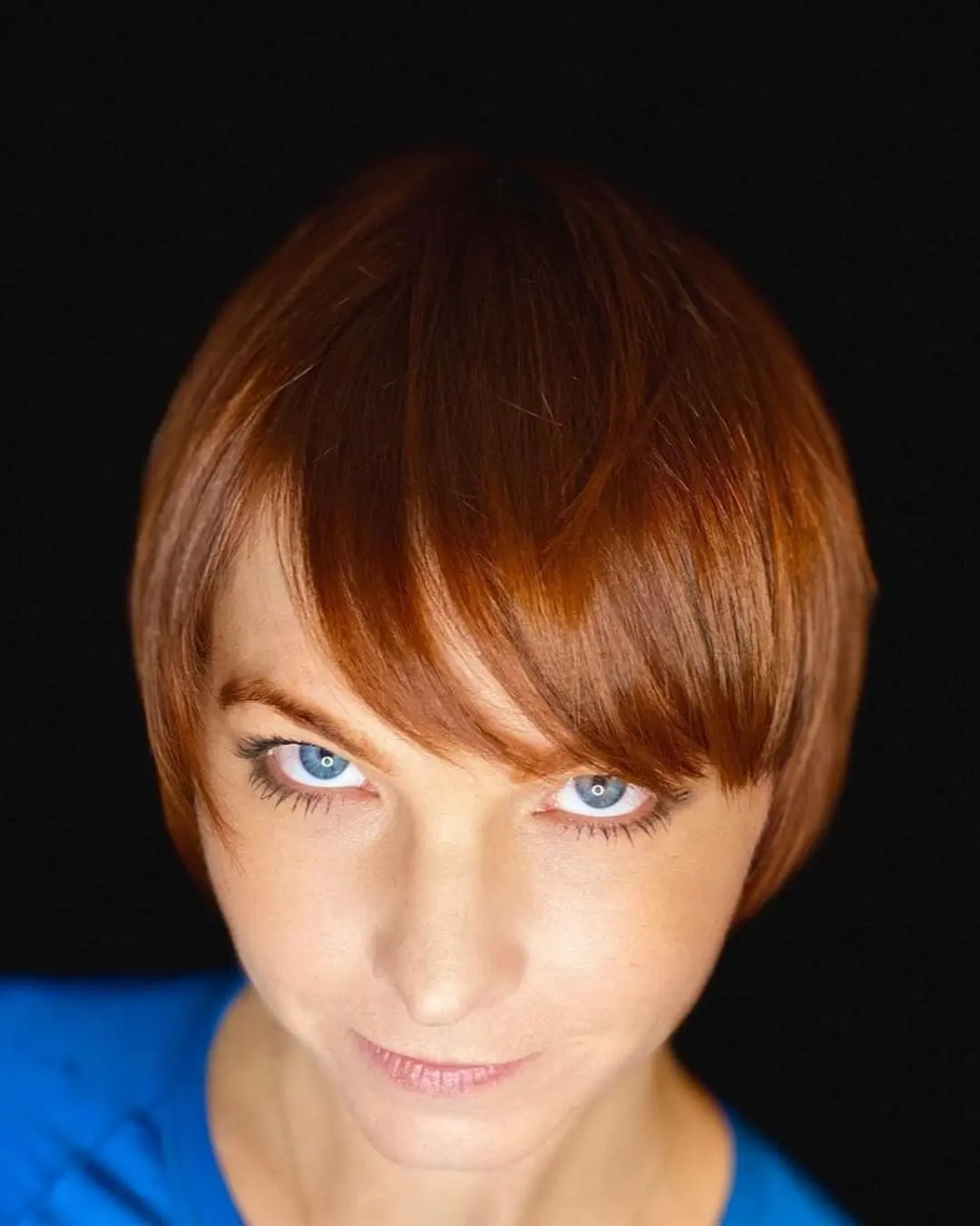 Lisa Edwards Portfolio 011 1080 x 1350 Close-up portrait of a woman with a sleek short pixie cut and sweeping front fringe, featuring a vibrant copper red all-over color by Lisa Edwards at Sunday Salon in Raleigh, NC.