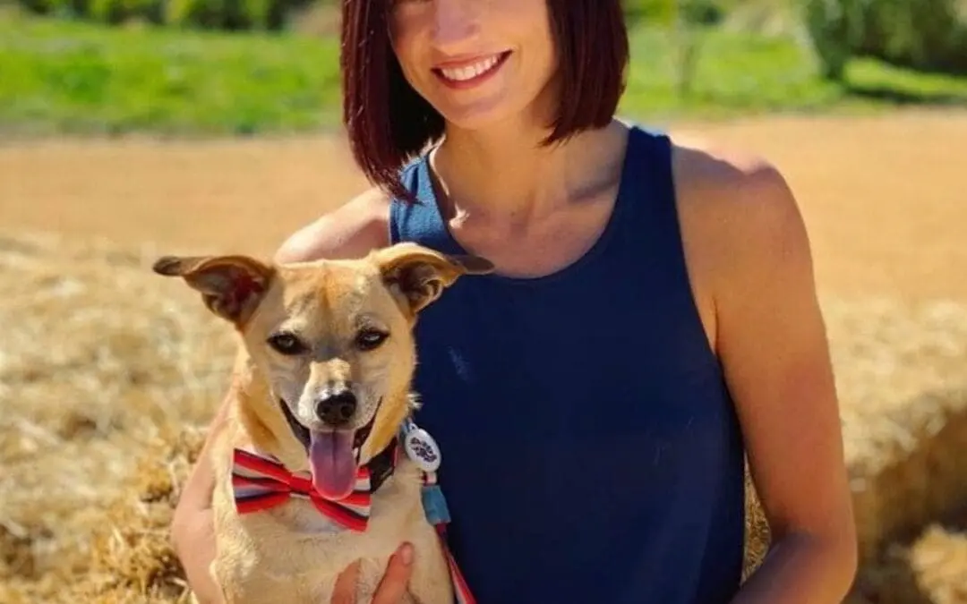 Portrait of a smiling woman outdoors holding a dog, featuring a sleek, chin-length bob and a rich, deep cherry auburn hair color by Lisa Edwards at Sunday Salon in Raleigh, NC.