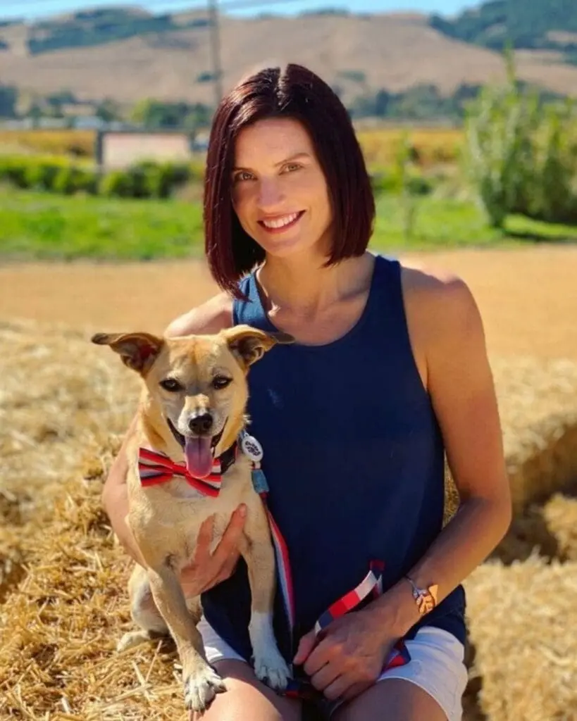 Portrait of a smiling woman outdoors holding a dog, featuring a sleek, chin-length bob and a rich, deep cherry auburn hair color by Lisa Edwards at Sunday Salon in Raleigh, NC.