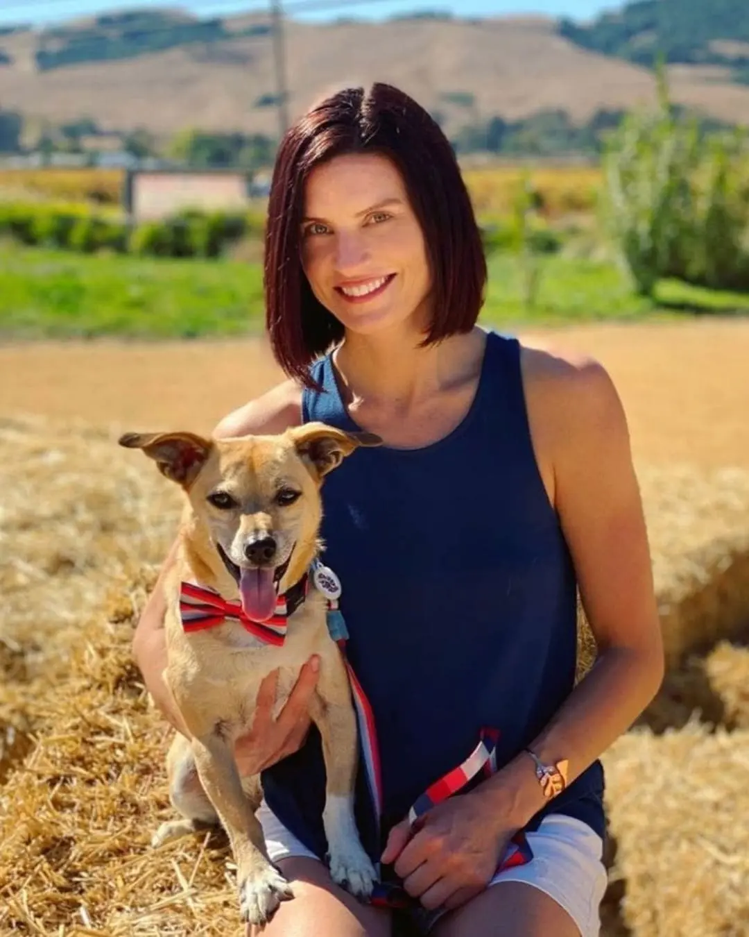 Deep Cherry Auburn All-Over Color on a Sleek Blunt Bob Portrait of a smiling woman outdoors holding a dog, featuring a sleek, chin-length bob and a rich, deep cherry auburn hair color by Lisa Edwards at Sunday Salon in Raleigh, NC.