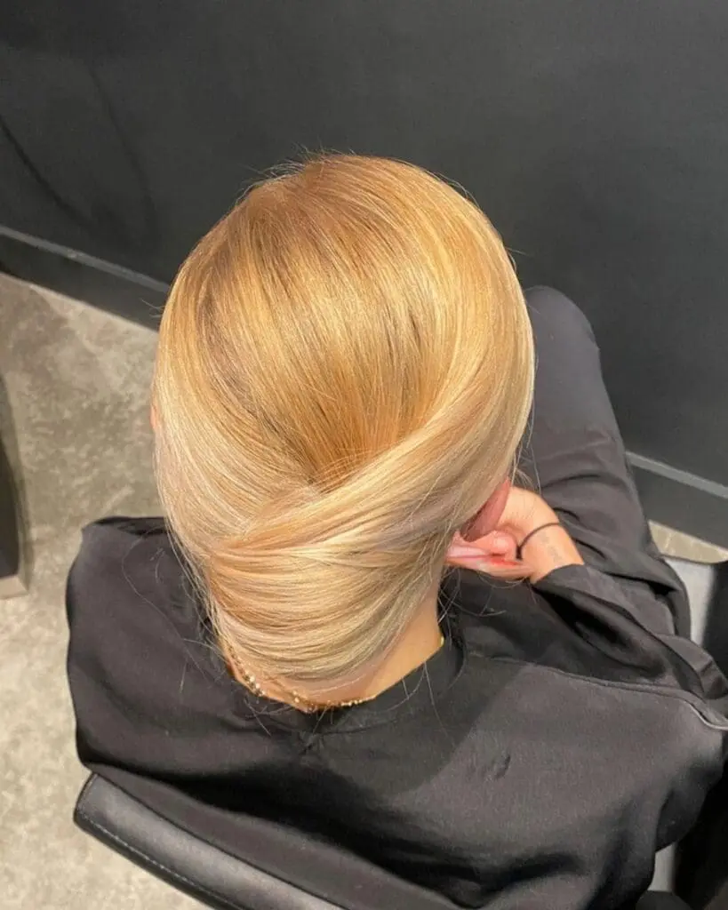 Top-down view of a woman with warm golden blonde hair styled in a smooth, elegant French twist low updo at Sunday Salon in Raleigh, NC.