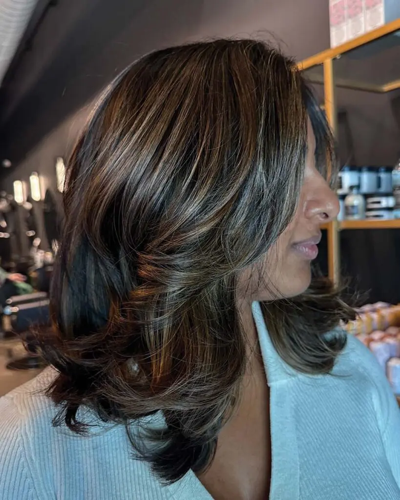 Dimensional Caramel Brunette with Voluminous Layers Medium-length deep brunette hair styled in a sleek, voluminous blowout with dimensional warm caramel highlights and face-framing layers, crafted by an expert stylist at Sunday Salon in Raleigh.