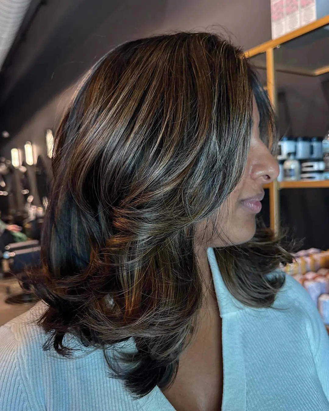 Medium-length deep brunette hair styled in a sleek, voluminous blowout with dimensional warm caramel highlights and face-framing layers, crafted by an expert stylist at Sunday Salon in Raleigh.