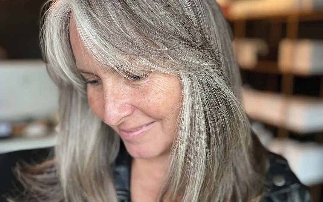 Medium-length sleek hair showcasing a sophisticated silver grey blending transformation with bright, face-framing highlights, crafted by an expert stylist at Sunday Salon in Raleigh.