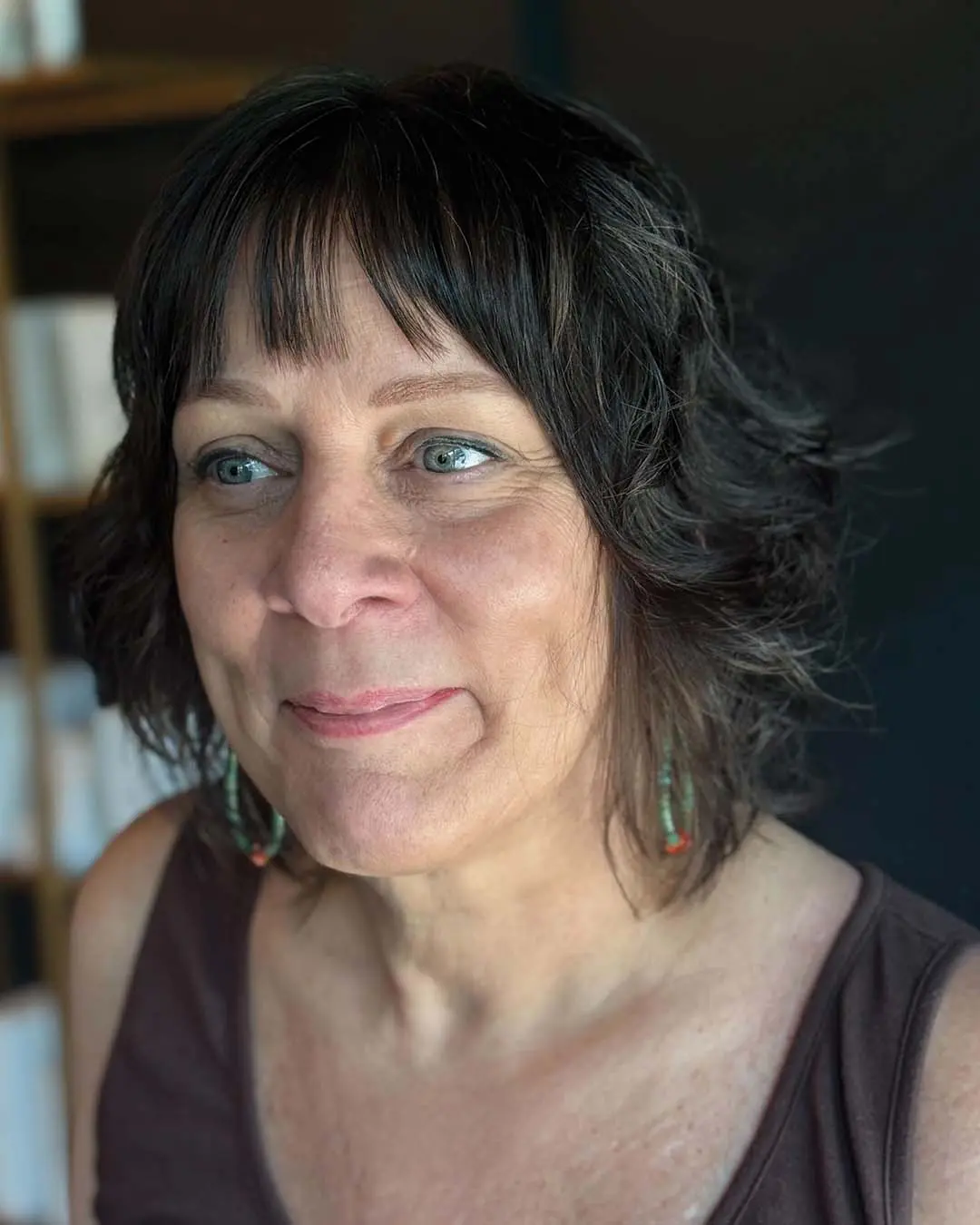 A chic, collarbone-length dark brunette shag haircut featuring soft textured waves and wispy, piecey bangs, custom crafted by an expert stylist at Sunday Salon in Raleigh.