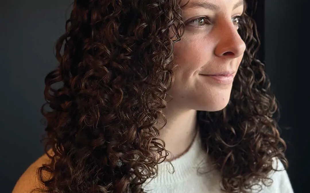 Medium-length, naturally curly hair styled with perfectly defined, bouncy ringlets in a rich chocolate brown hue with warm undertones, expertly shaped by a stylist at Sunday Salon in Raleigh.