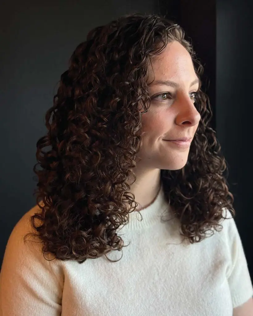 Voluminous Chocolate Brown Defined Curls Medium-length, naturally curly hair styled with perfectly defined, bouncy ringlets in a rich chocolate brown hue with warm undertones, expertly shaped by a stylist at Sunday Salon in Raleigh.