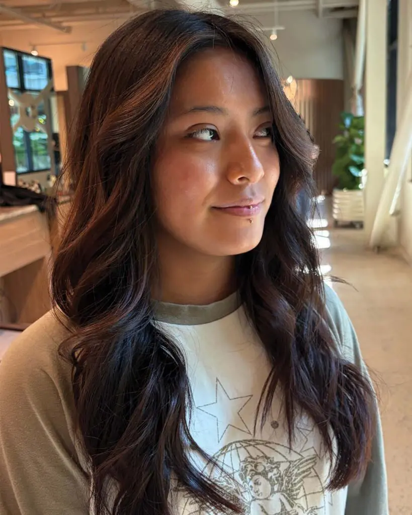 Deep Espresso Brunette with Warm Auburn Face-Framing Ribbons A long, thick deep espresso brunette haircut styled with soft, voluminous waves and subtle warm auburn face-framing highlights, created at Sunday Salon in Raleigh.