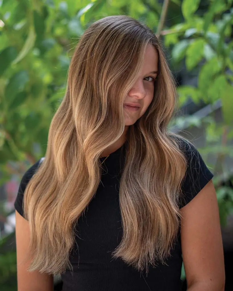 Lived-In Warm Honey Balayage with Soft Cascading Waves A long, thick hair transformation featuring seamless warm honey balayage, subtle golden highlights, and soft cascading waves created at Sunday Salon in Raleigh.