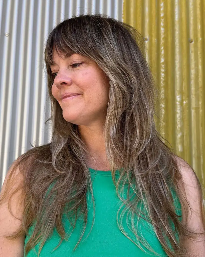 Muted Ash Dimensional Balayage with Full Curtain Bangs and Shag Layers A long ash brunette hair transformation featuring subtle dimensional highlights, full curtain bangs, and soft shaggy face-framing layers created at Sunday Salon in Raleigh.