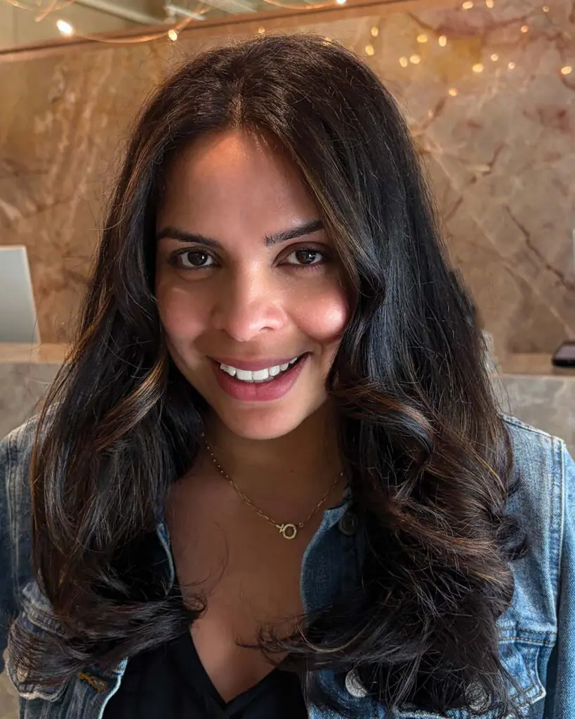 Rich Dark Chocolate Brunette with Soft Warm Caramel Ribbons A long, thick dark chocolate brunette haircut styled with glamorous voluminous waves and subtle warm caramel highlights, crafted at Sunday Salon in Raleigh.