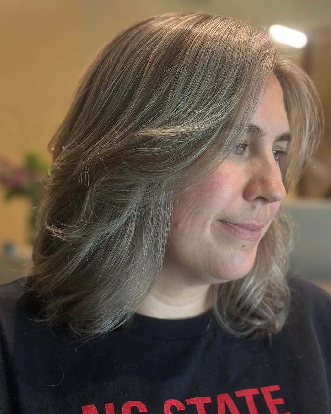 A medium-length silver and ash brown dimensional haircut styled with soft, face-framing layers and a polished blowout finish created at Sunday Salon in Raleigh.