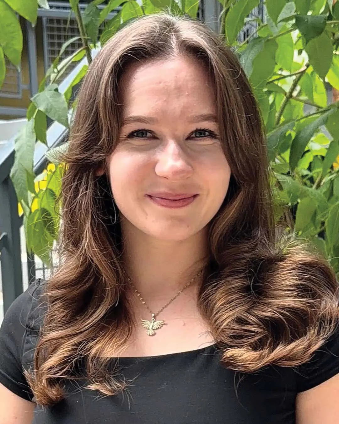 A medium-to-long chestnut brunette hair transformation created at Sunday Salon in Raleigh, featuring soft curtain bangs, warm caramel ribbon highlights, and a voluminous bouncy wave style.