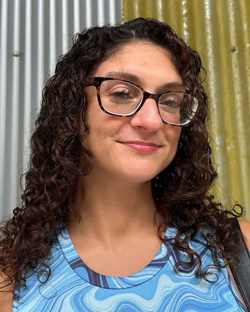 A smiling woman displaying shoulder-length, defined dark chestnut curly hair with subtle warm highlights styled at Sunday Salon in Raleigh.