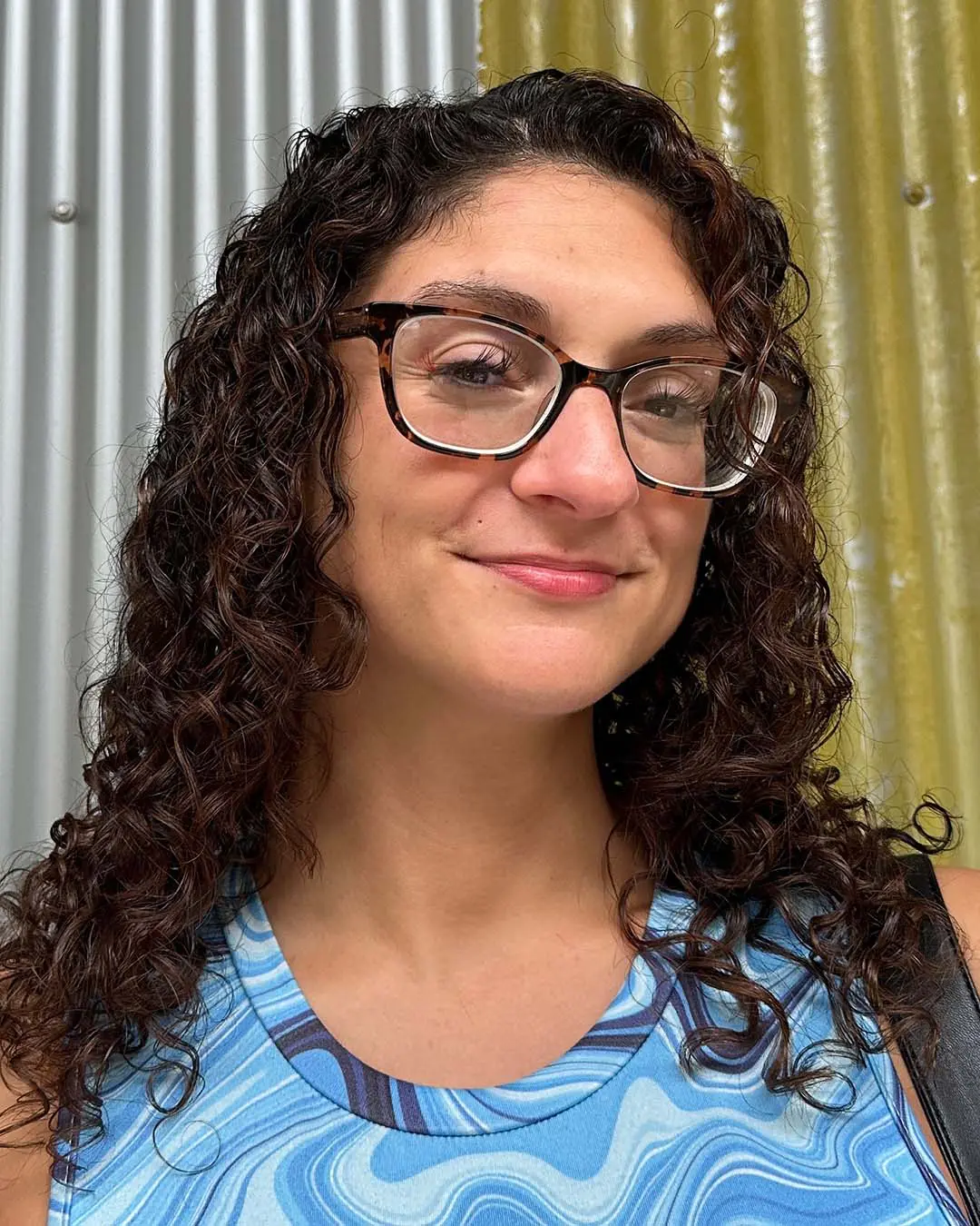 A smiling woman displaying shoulder-length, defined dark chestnut curly hair with subtle warm highlights styled at Sunday Salon in Raleigh.