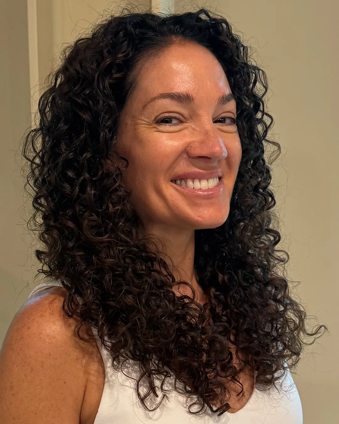 A smiling woman showcasing defined dark espresso curly hair with medium length, styled impeccably at Sunday Salon in Raleigh.