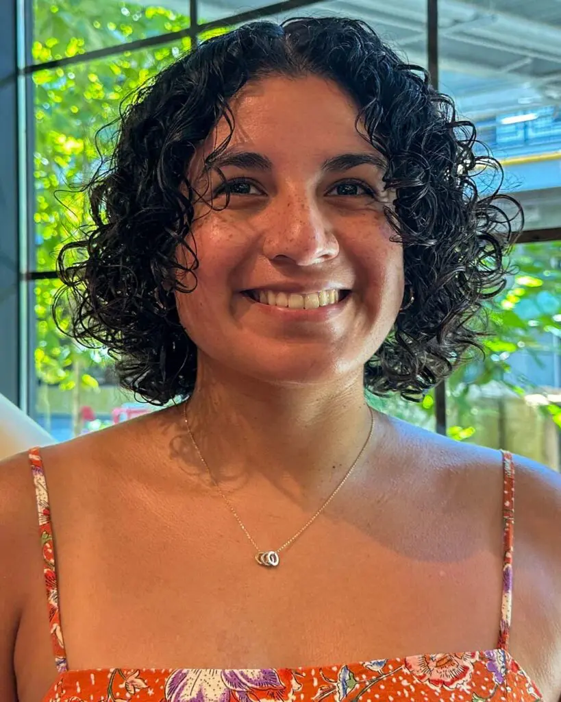 A smiling woman showing off a chin-length deep espresso curly haircut with springy defined ringlets, expertly styled at Sunday Salon in Raleigh.