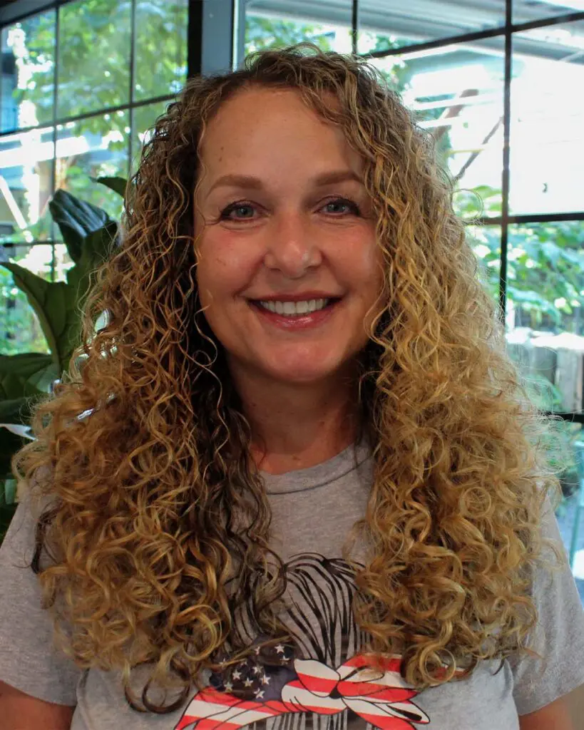 Shoulder-length blonde hair with extremely defined, springy curls and lighter highlights, created by expert stylists at Sunday Salon in Raleigh.