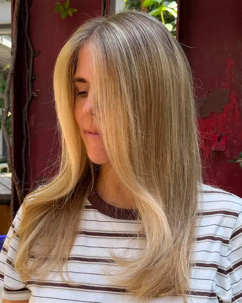 A woman displaying long, straight beige blonde hair with face-framing bright money piece highlights styled at Sunday Salon in Raleigh.