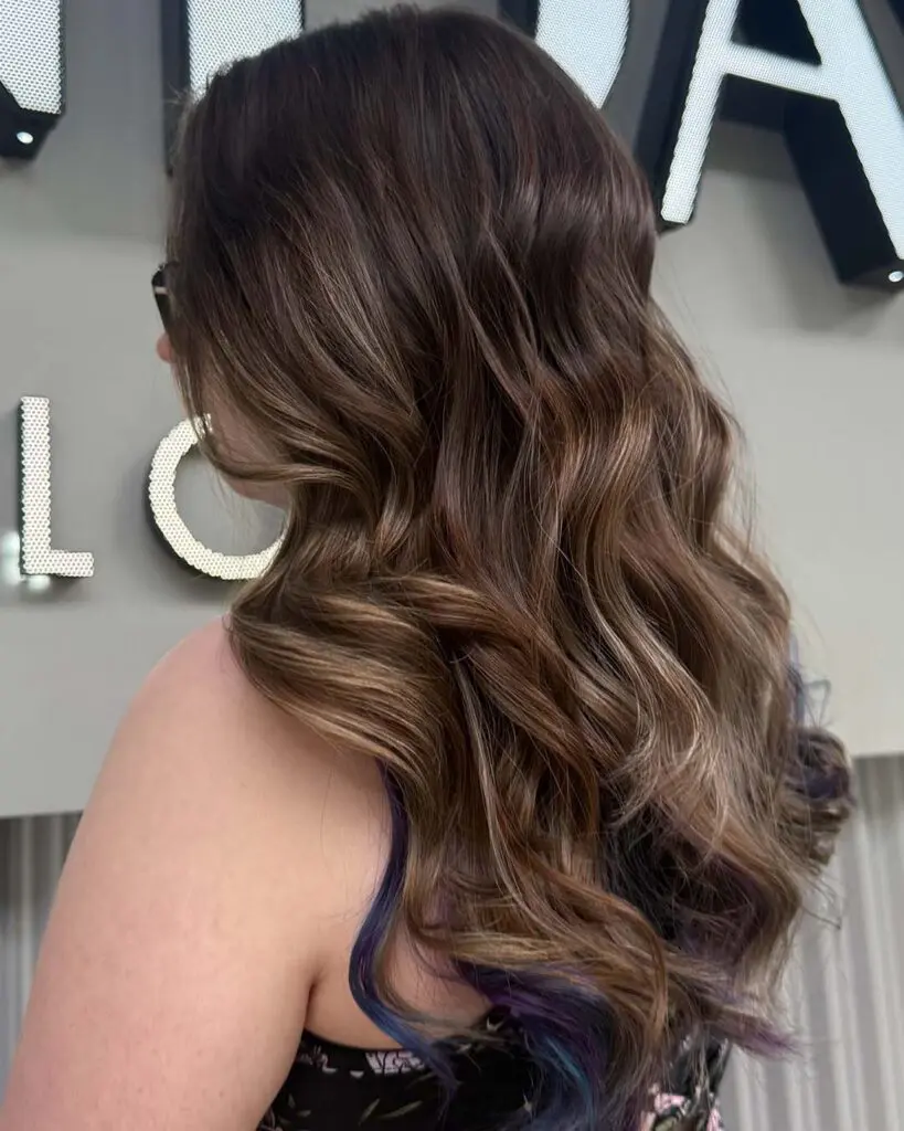 A side-back view of mid-length cascading mocha waves revealing a hidden violet peekaboo highlight underneath, styled expertly at Sunday Salon in Raleigh.