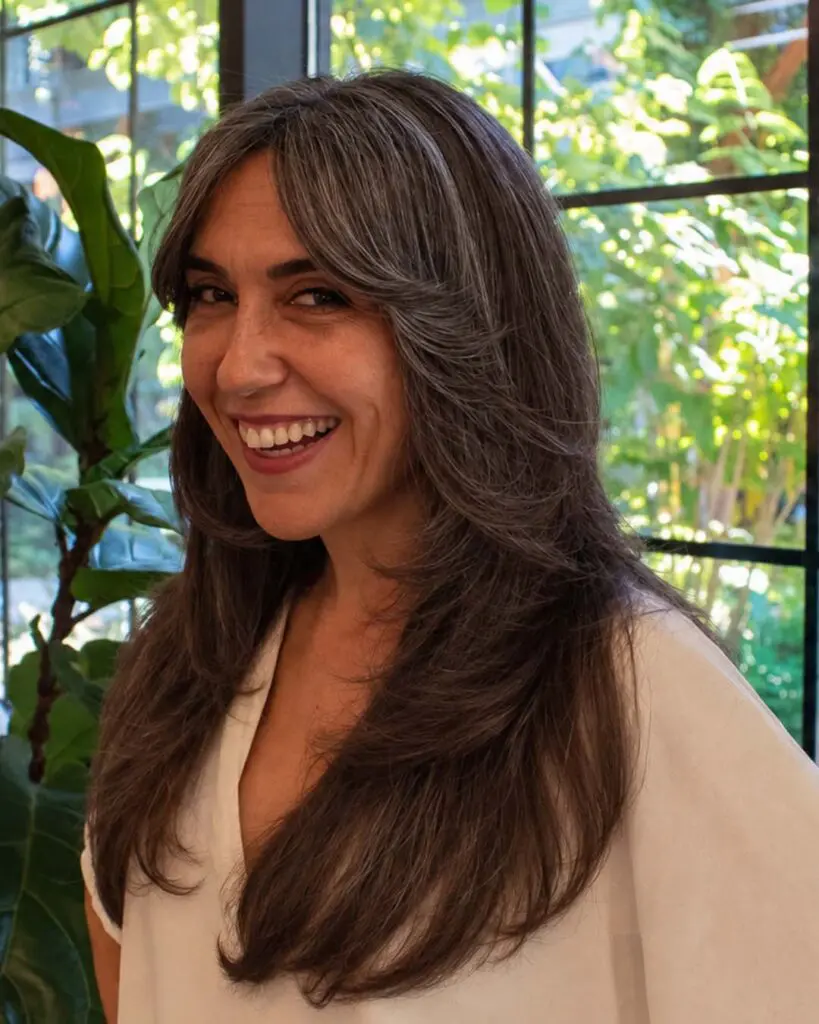 Long, flowing salt-and-pepper silver hair with smooth feathered face-framing layers crafted at Sunday Salon located in Raleigh.