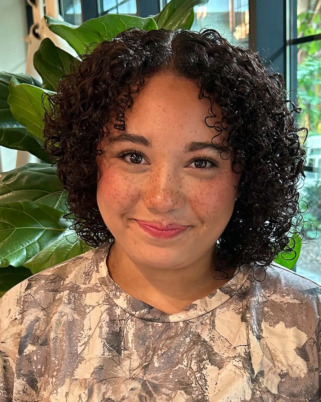 A smiling woman showing off a shoulder-length, dark chocolate curly bob with tight, shiny ringlets styled at Sunday Salon in Raleigh.