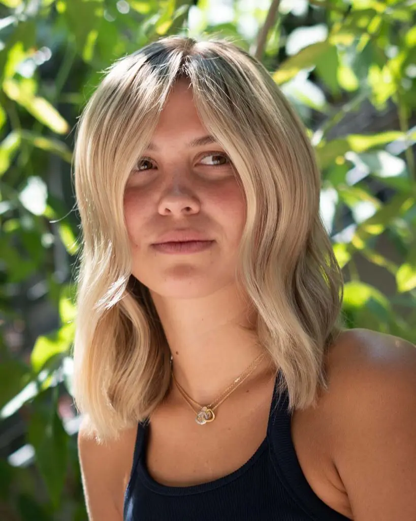 A portrait of a woman displaying a shoulder-length butter blonde lob with curtain bangs and soft waves styled at Sunday Salon in Raleigh.