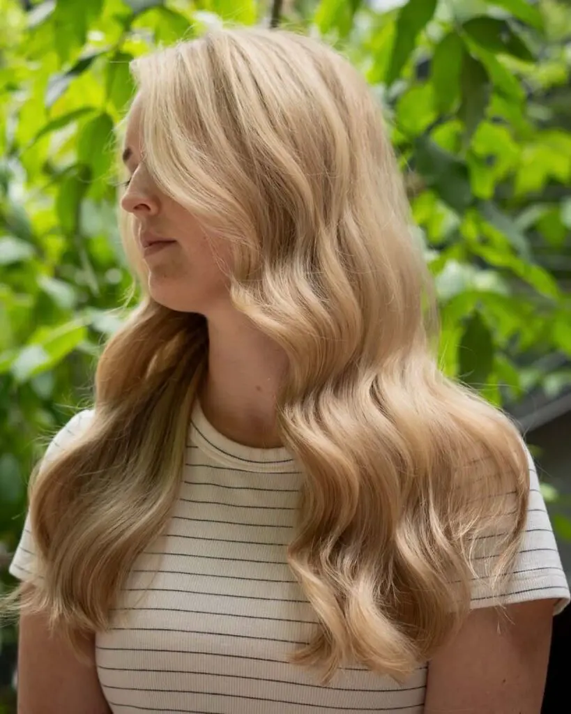 Luminous Golden Blonde Hollywood Waves with Soft Face-Framing Fringe A side profile of a woman showcasing long, cascading golden blonde glam waves with soft face-framing fringe styled at Sunday Salon in Raleigh.