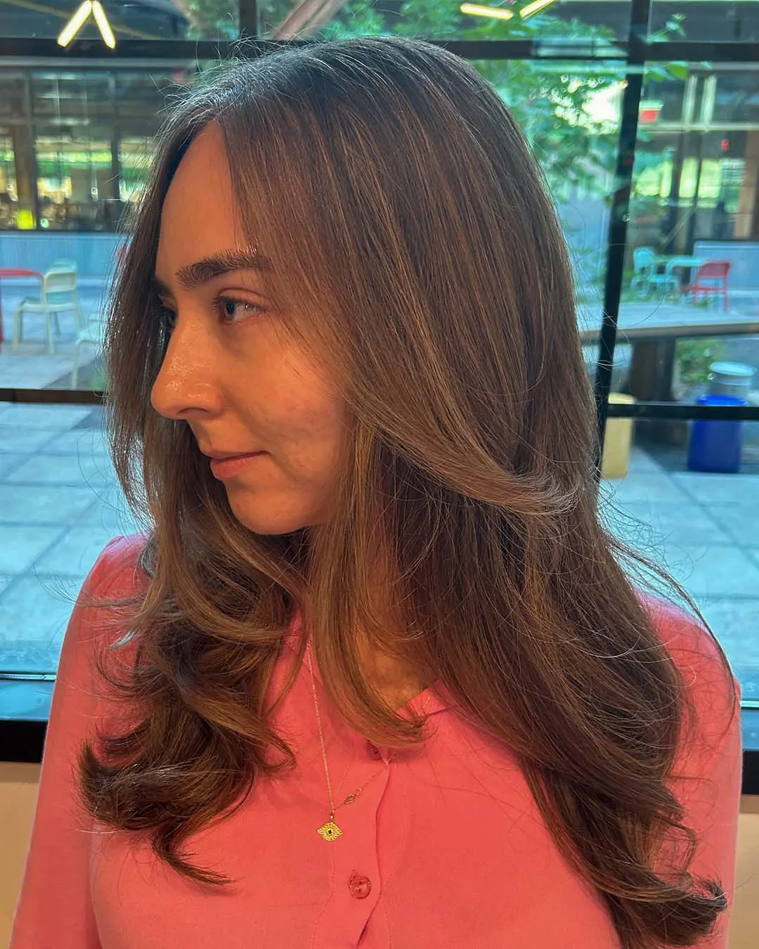 A side view of a woman featuring long, soft chestnut waves with seamless highlights and face-framing curtain bangs styled at Sunday Salon in Raleigh.