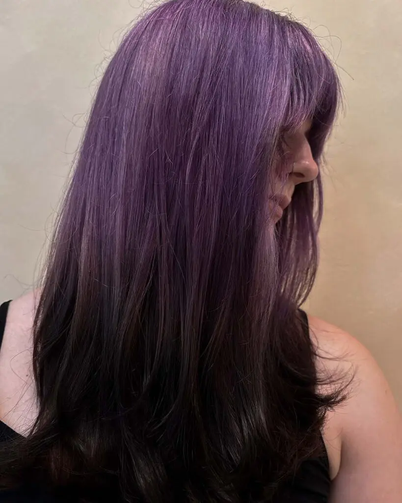 A profile view of long straight hair featuring a muted lavender crown melting into dark espresso ends with a full fringe, styled at Sunday Salon in Raleigh.