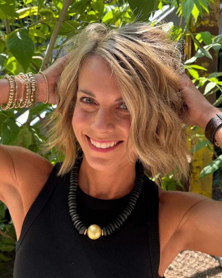 A smiling woman posing outdoors showing off a textured, chin-length golden blonde crop with lived-in highlights styled by Sunday Salon in Raleigh.