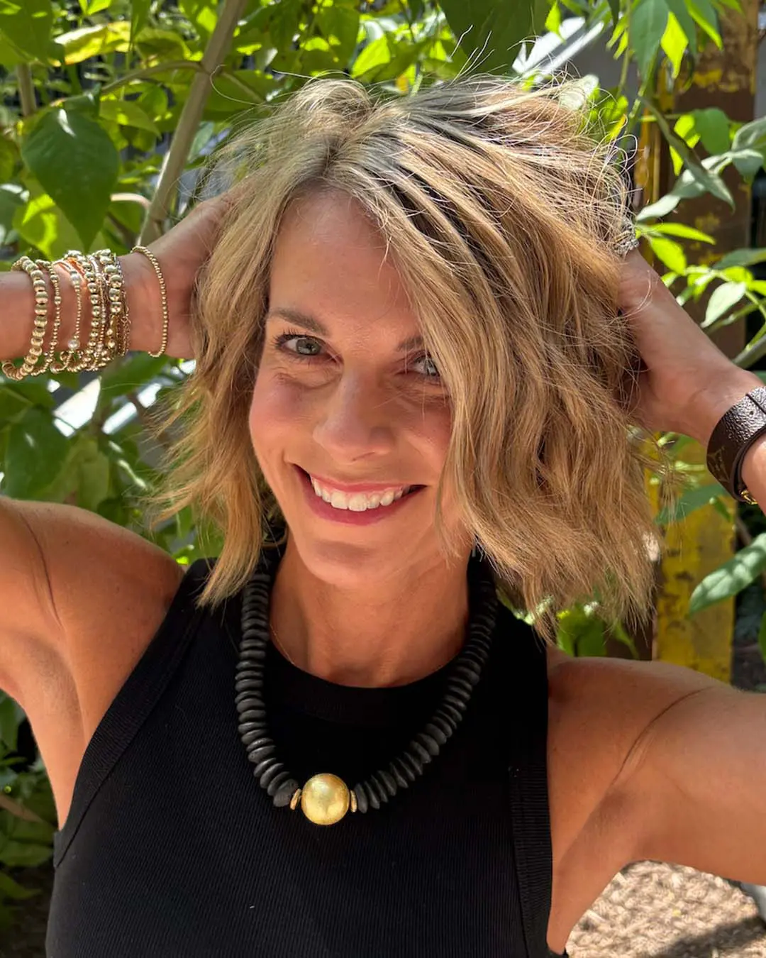 Textured Golden Blonde Crop with Lived-in Dimension A smiling woman posing outdoors showing off a textured, chin-length golden blonde crop with lived-in highlights styled by Sunday Salon in Raleigh.