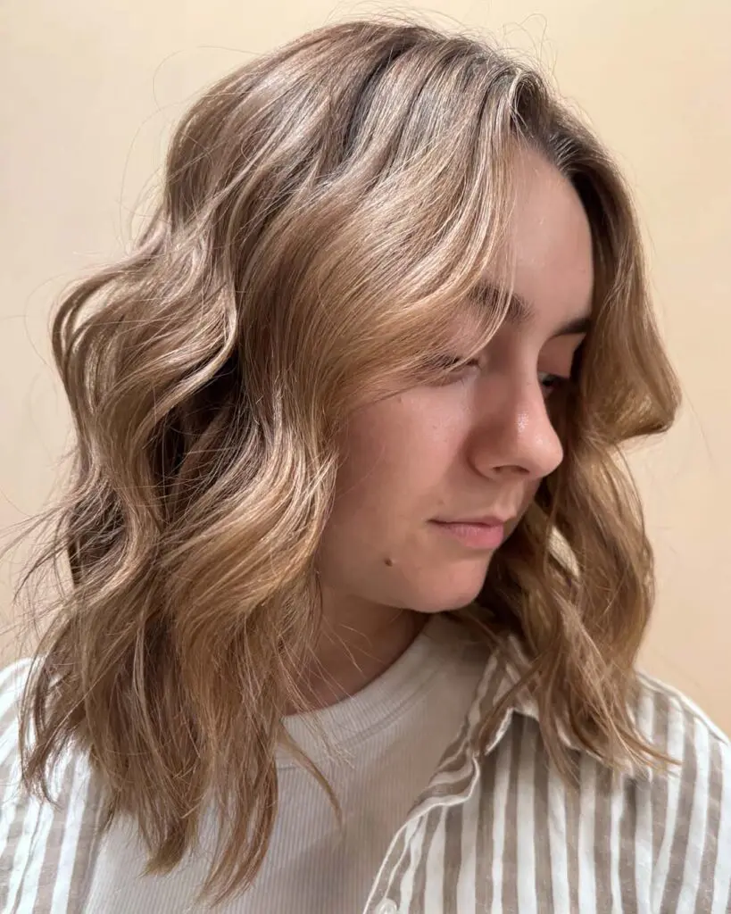 A woman showing off a shoulder-length shoulder-grazing honey blonde lob with beachy waves crafted by a stylist at Sunday Salon in Raleigh.