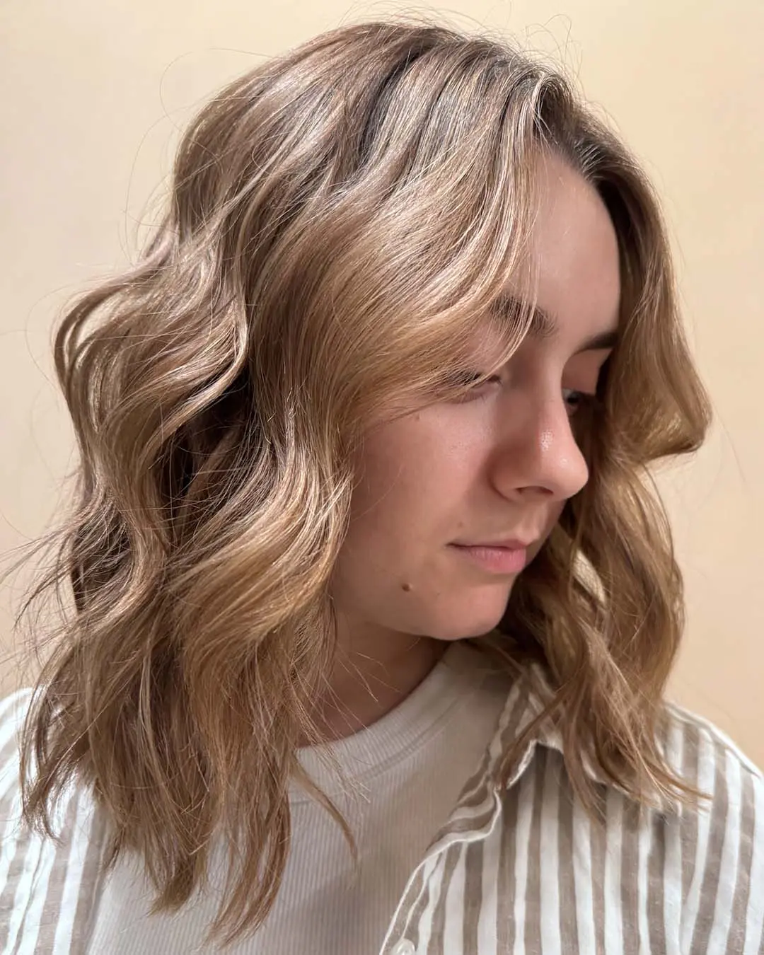Warm Honey Blonde Lived-In Lob with Effortless Waves A woman showing off a shoulder-length shoulder-grazing honey blonde lob with beachy waves crafted by a stylist at Sunday Salon in Raleigh.