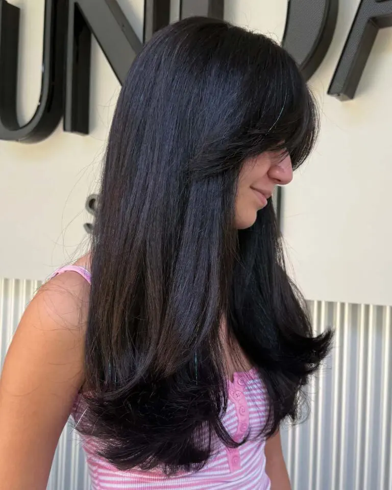 A person with long, straight, espresso hair featuring face-framing layers and curtain bangs.
