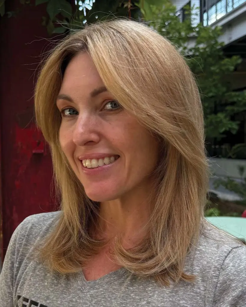 Client showcasing a warm honey blonde dimensional lob with soft curtain bangs and subtle flipped ends created at Sunday Salon in Raleigh.
