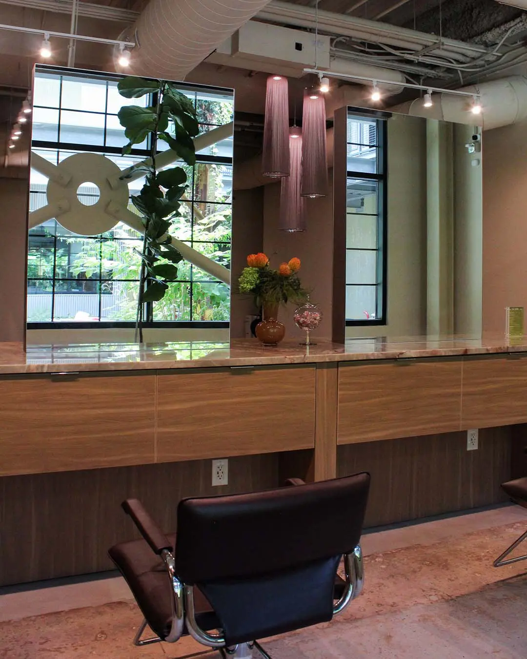 color room image 1 A hair salon station featuring a long wood-toned counter with mirrors, a black styling chair, and a vase of orange flowers.