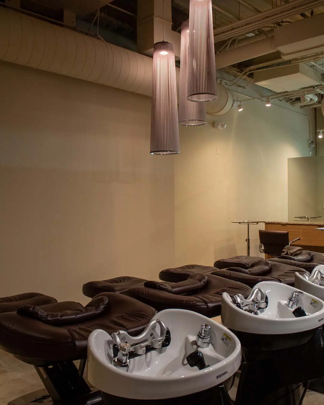 color room image 2 A row of salon shampoo bowls with attached reclining chairs under hanging pendant lights.