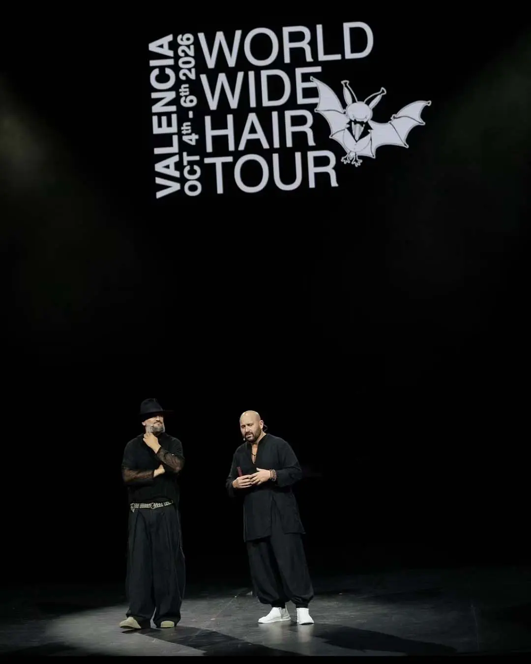 davines-europe-5 Two men in black clothing stand on a dark stage beneath a projected logo for the World Wide Hair Tour in Valencia, October 4th–6th, 2026.